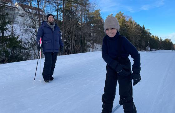 Gutt som st&aring;r p&aring; ski med faren i bakgrunn.