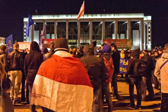 Et kveldsbilde, hvor hviterussiske demonstranter er samlet p&aring; et torg og b&aelig;rer det hvite og r&oslash;de flagget deres.