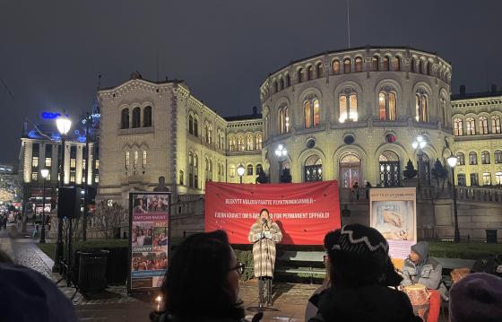 Bildet viser Khansa Ali som st&aring;r foran Stortinget og holder en appell. Bak henne henger det et r&oslash;dt banner hvor det st&aring;r "Beskytt voldsutsatte flyktningkvinner - fjern kravet om 5 &aring;rs botid for permanent opphold".