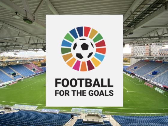 Bilde av en stadio, hvor det er limt p&aring; en hvit boks over med logoen til Football for the goals. Det er b&aelig;rekraftsfargene i en sirkel rundt en fotball.