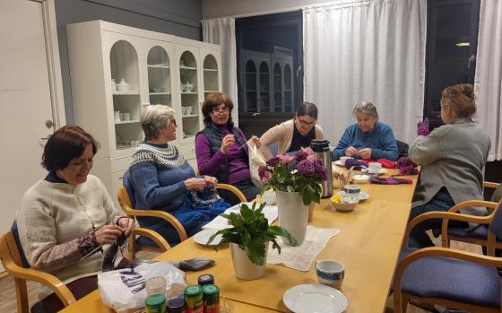 Seks damer p&aring; Sagene Frivilligsentral sin strikkekaf&eacute;, som sitter rundt et bord og drikker kaffe og strikker.