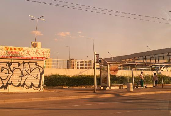 En gate i Bulgaria om sommeren. Det er kun to mennesker p&aring; busstoppet.
