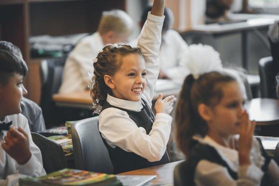smilende skolepike rekker opp h&aring;nden i klasserommet