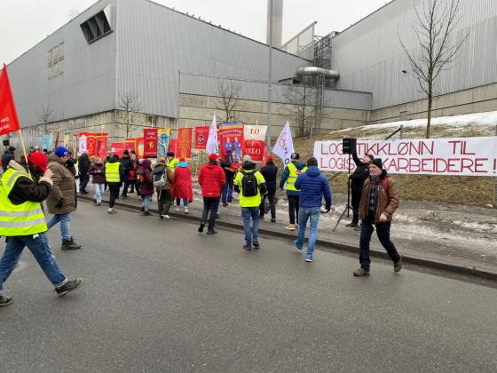 Mennesker g&aring;r over veien, skilt og bannere i bakgrunnen