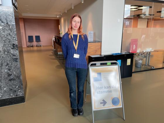Valgmedarbeider Sunniva Harstein st&aring;r bak en plakat med teksten "Her kan du stemme".