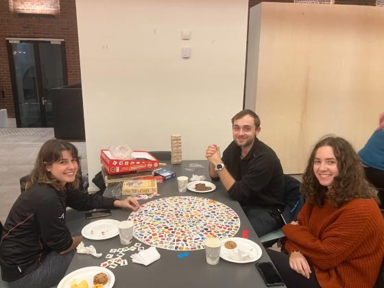 Bord med tre studenter rundt, p&aring; bordet ligger noen brettspill og papptallerkner med snacks