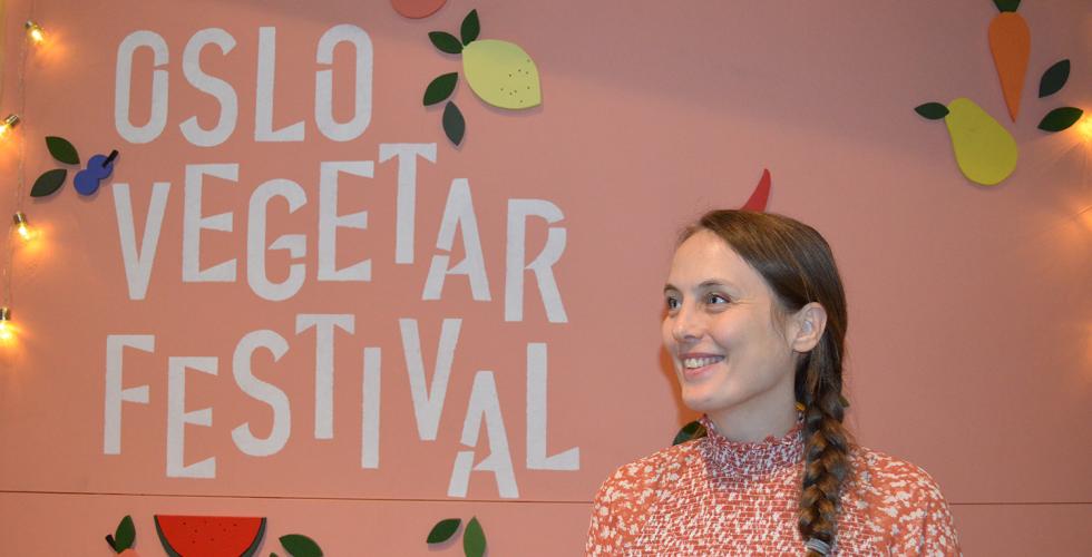 Ung kvinne st&aring;r foran Oslo Vegetarfestival-skilt og smiler