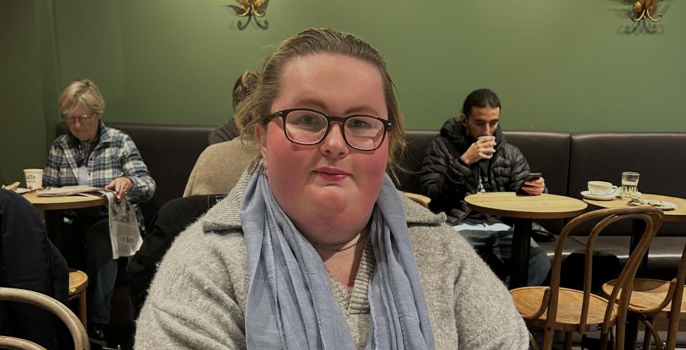 en jente sitter i et kafelokale med bl&aring;tt skjerf
