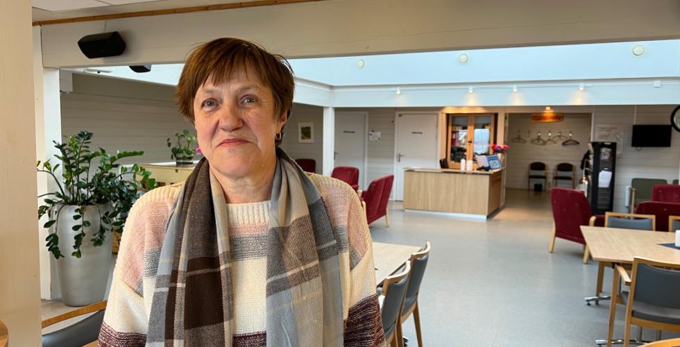 Dame med skjerf, smiler, st&aring;r i en kantine