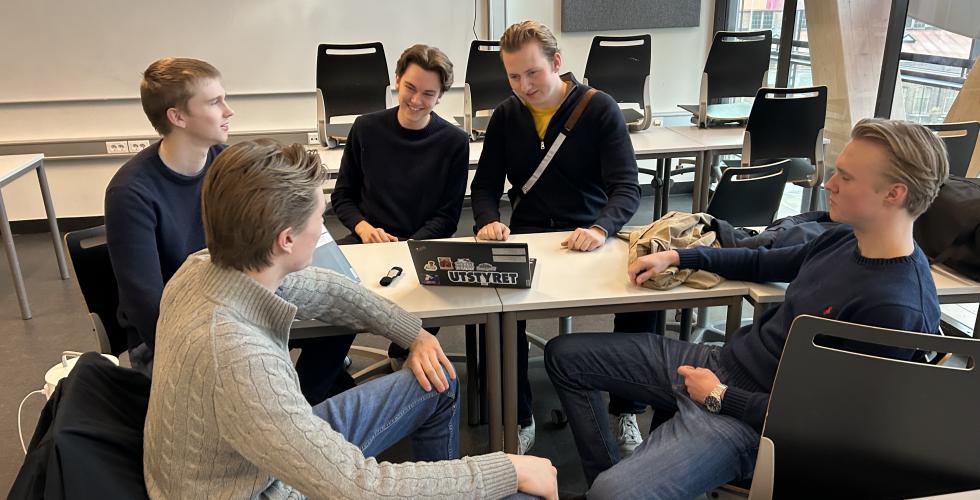 Unge gutter sitter ved en pult og snakker om ungdomsbedriften sin