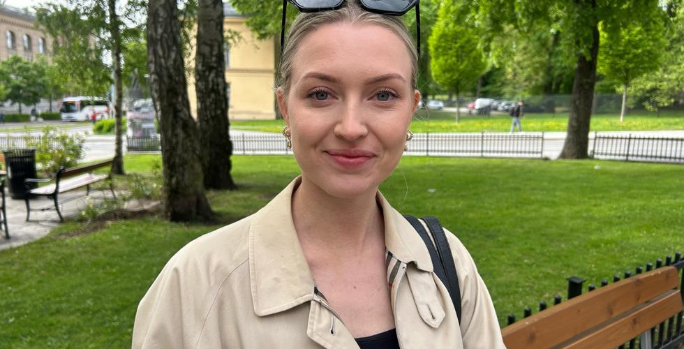 Ung dame som smiler til kamera mens hun venter p&aring; bussen.