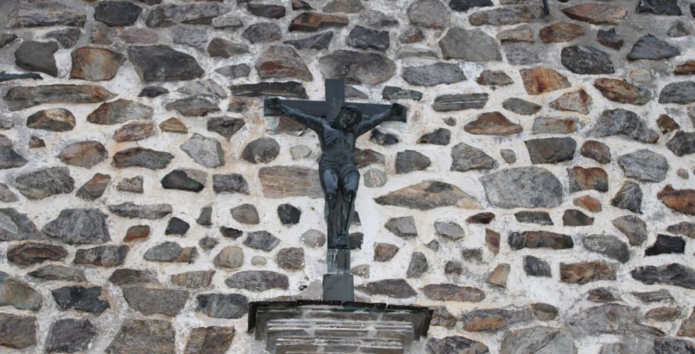 P&aring; en steinvegg, henger et kors med Jesus p&aring;