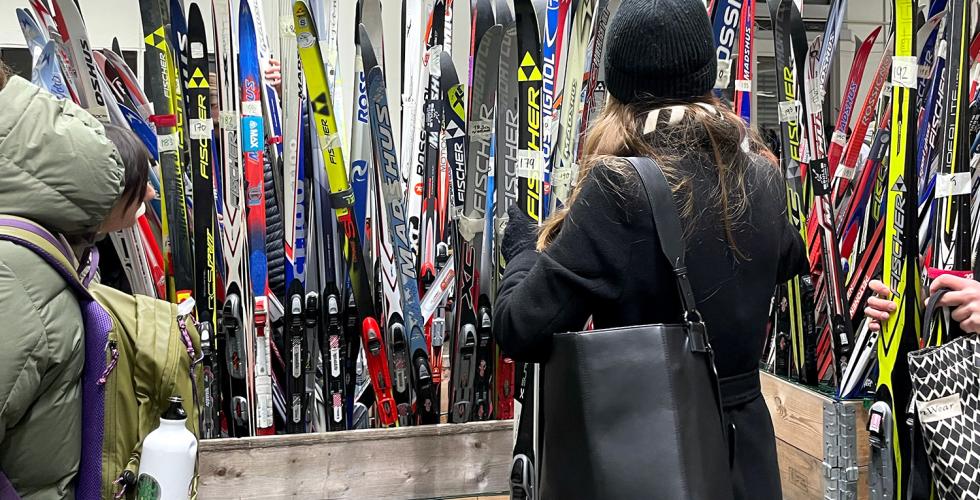Mange langrennski st&aring; rett opp og ned i en kasse. En kvinne st&aring;r forran kassen og holder et parr med langrennsski
