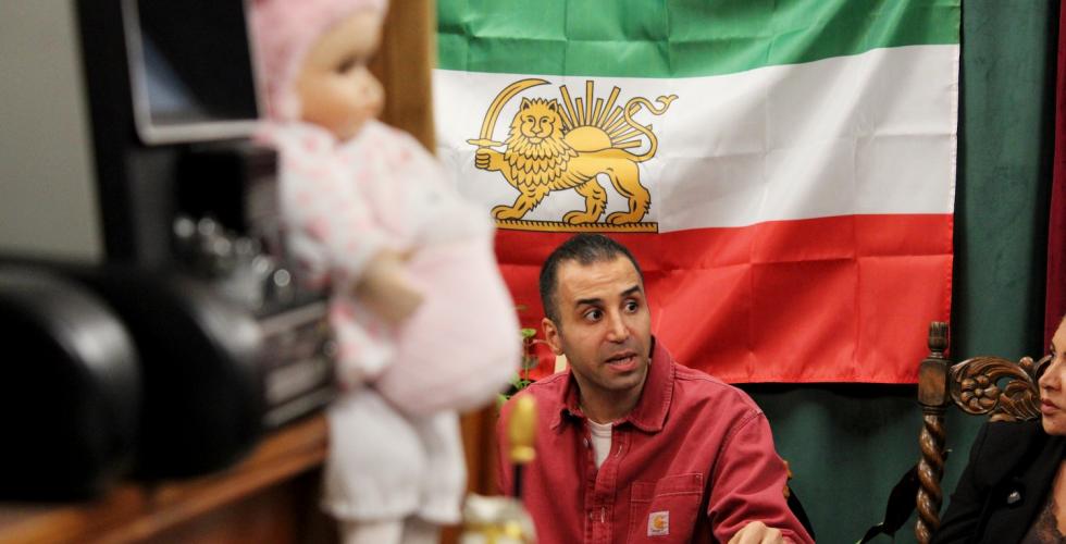 En mann sitter &aring; diskuterer foran et Iransk flagg