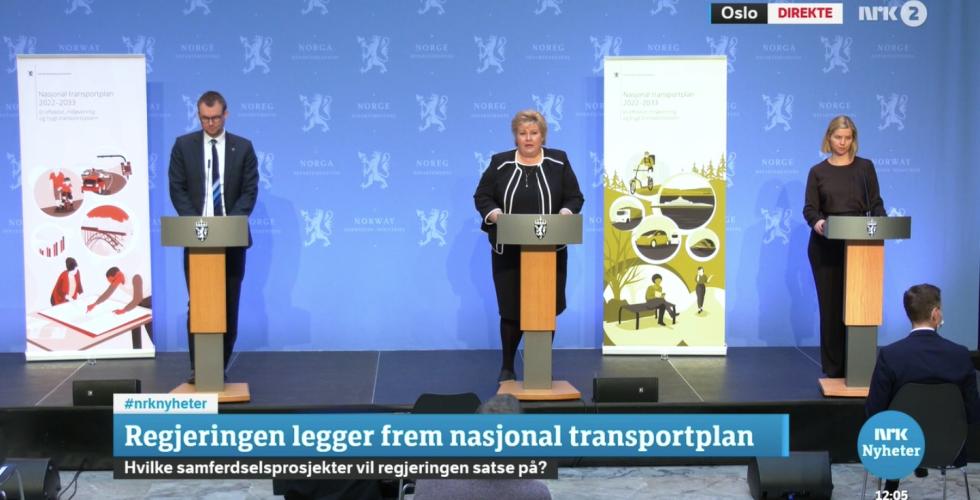 Erna Solberg, Guri Melbye, og Knut Arild Hareide st&aring;r ved siden av hverandre p&aring; et podium, og legger frem den nasjonale transportplanen for 2022-2033.