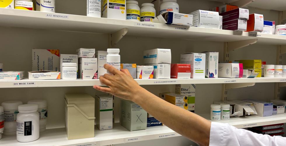 Bilde av medisiner og en h&aring;nd som strekker seg mot en eske med medisin