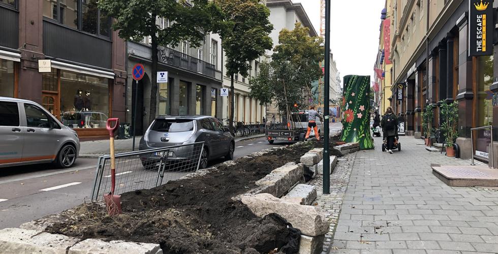Tr&aelig;r b&aelig;res p&aring; en tilhenger ved siden av det tomme blomsterbedet
