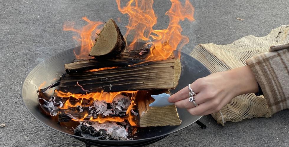 Bilde av et b&aring;l som brenner, med en h&aring;nd som stikker en lapp inn i b&aring;let.
