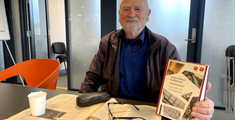 mann holder opp boka han har l&aring;nt mens han drikker kaffe og leser dagens avis