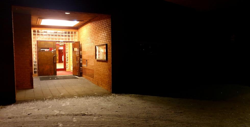 Inngangsparti til en kirke i murstein, d&oslash;ren er &aring;pen og det er lyst inne, mens det er helt m&oslash;rkt utenfor