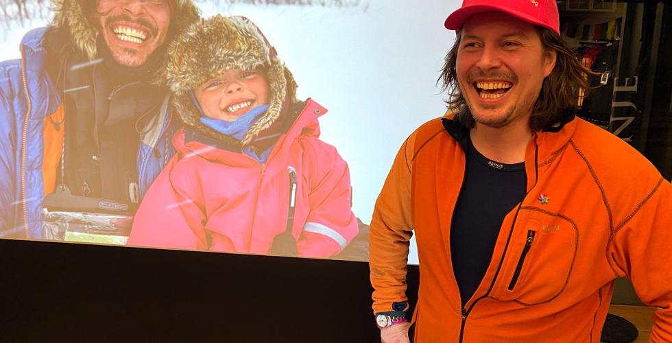 Alexander Read fra Mina og Meg st&aring;r foran skjerm med bilde av han og Mina