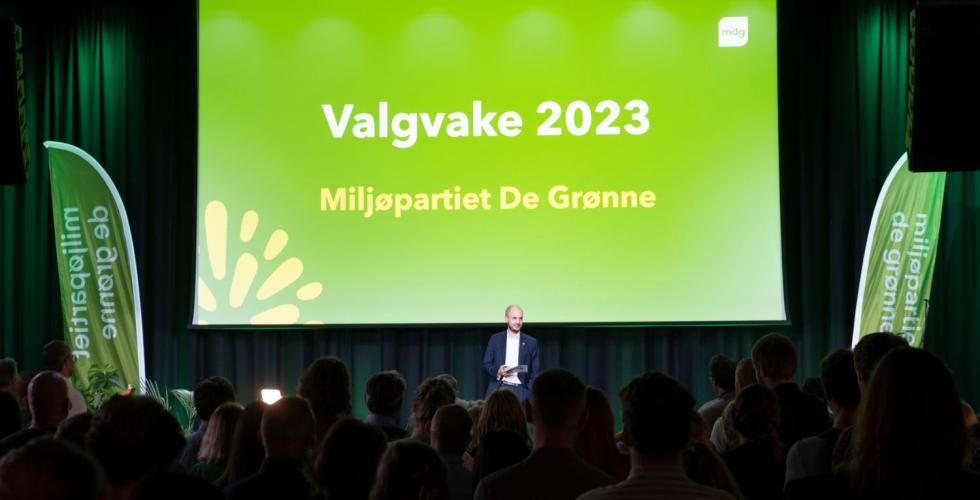 P&aring; bildet ser man publikum foran en scene og skjerm lyst opp med en gr&oslash;nn bakgrunn og MDGs logo