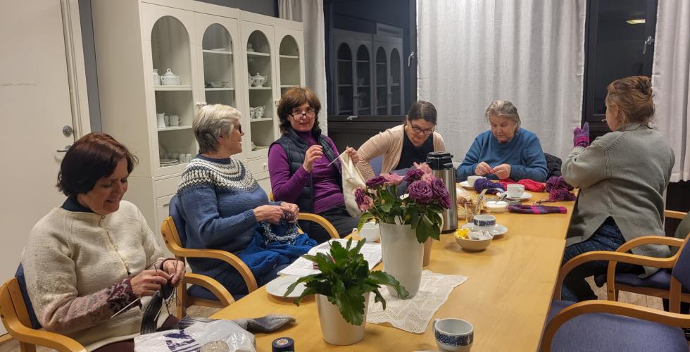 Seks damer p&aring; Sagene Frivilligsentral sin strikkekaf&eacute;, som sitter rundt et bord og drikker kaffe og strikker.