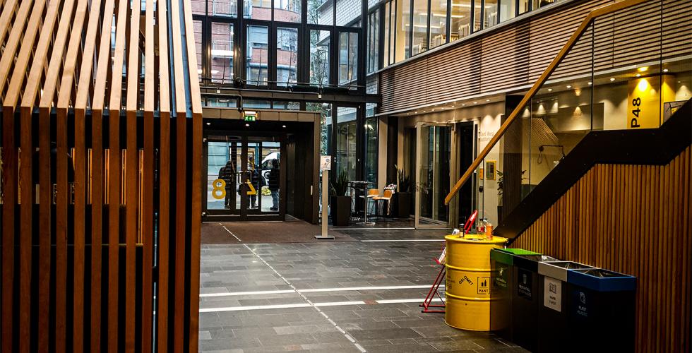 Bildet viser hovedinngangen av et skole bygg p&aring; Oslomet. Det er et &aring;pent inne omr&aring;de med mange glassvinduer som strekker seg flere etasjer opp, og flere klasserom
