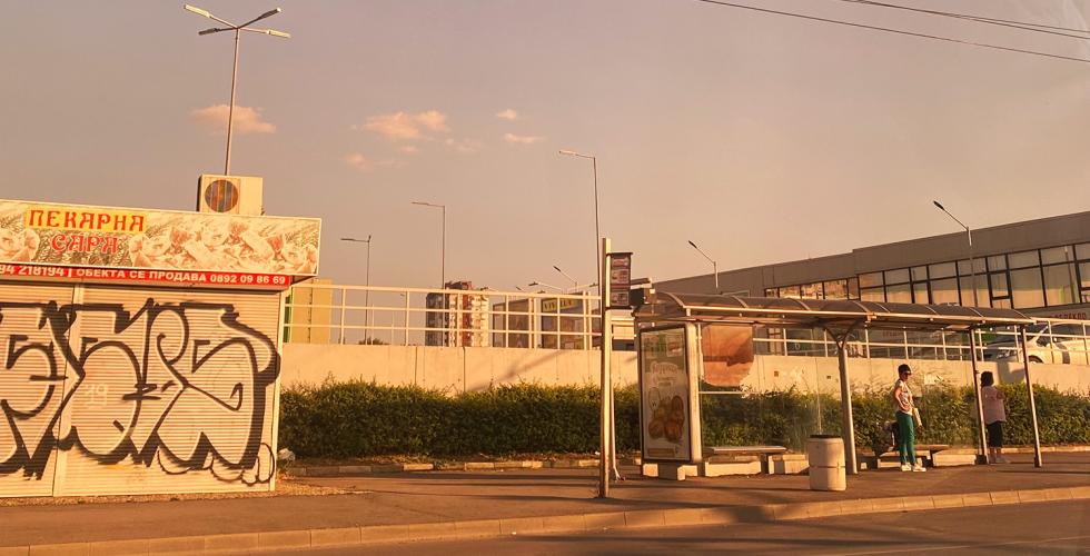En gate i Bulgaria om sommeren. Det er kun to mennesker p&aring; busstoppet.