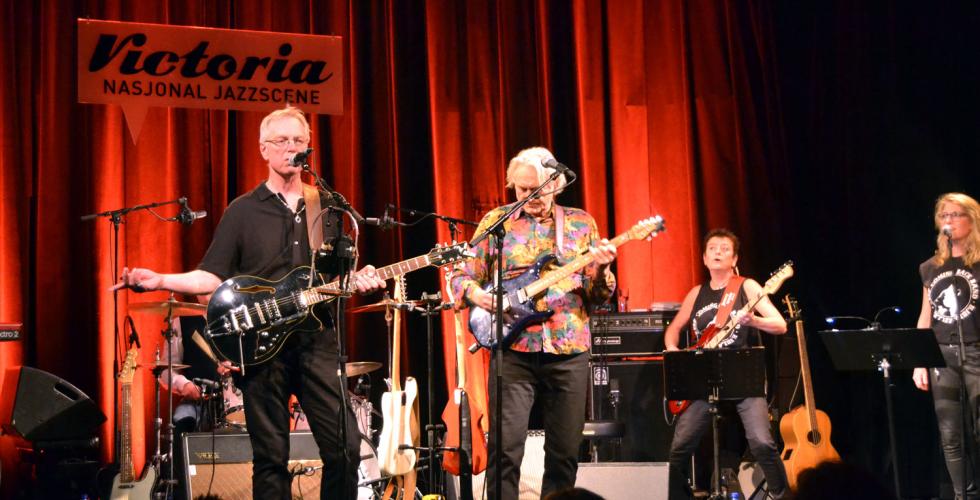 Bandet st&aring;r p&aring; scenen. Sigmund &Oslash;vrum synger mens Dag Vargseth spiller gitar. Rundt dem ser man de andre bandmedlemmene. 