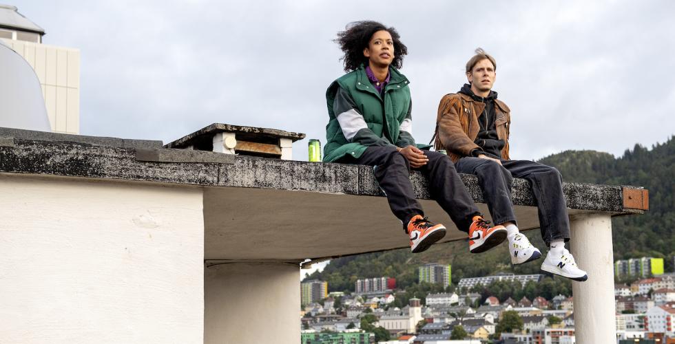 Hovedrollene Odilie og Stian sitter p&aring; et tak og ser utover Bergen by