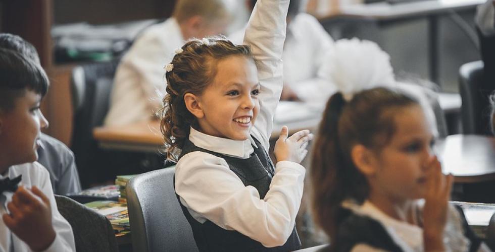 smilende skolepike rekker opp h&aring;nden i klasserommet
