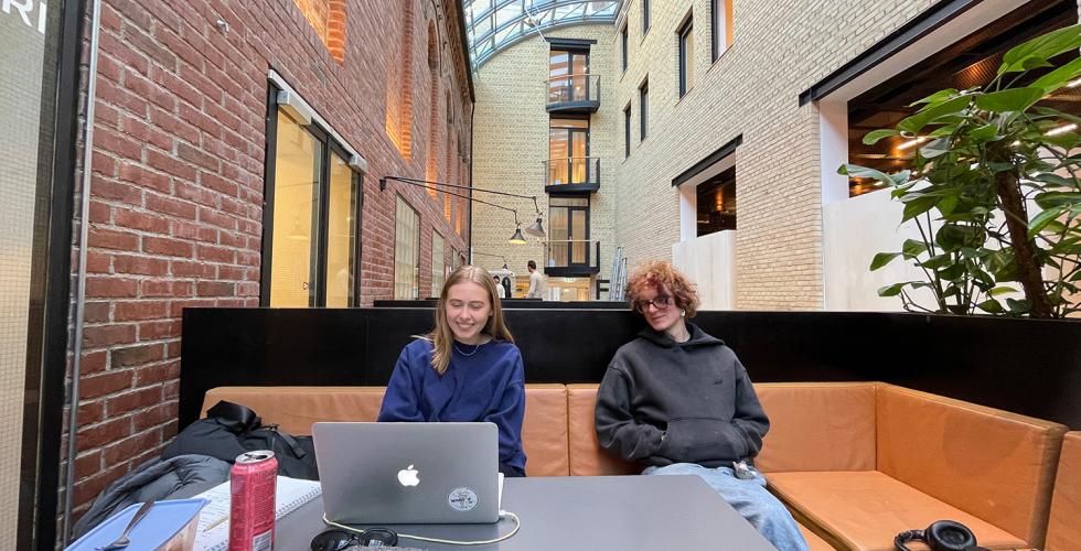 En gutt og ei jente sitter i en brun skinnsofa. De sitter i er et stort rom. Jenta smiler og gutten ser p&aring; henne. De er studenter. 