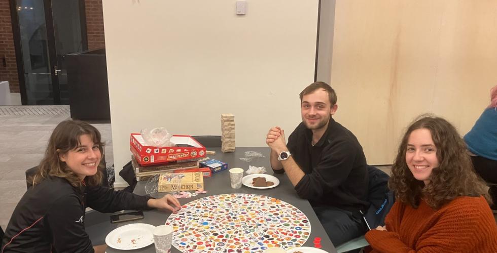 Bord med tre studenter rundt, p&aring; bordet ligger noen brettspill og papptallerkner med snacks