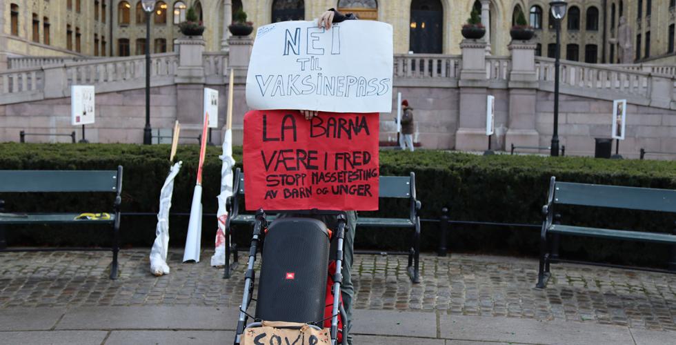 En demonstrant fra R&oslash;de Luer skjuler seg bak plakater mot vaksinepass