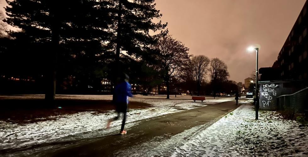 Det er m&oslash;rkt ute og mann jogger forbi p&aring; en vei med sn&oslash;